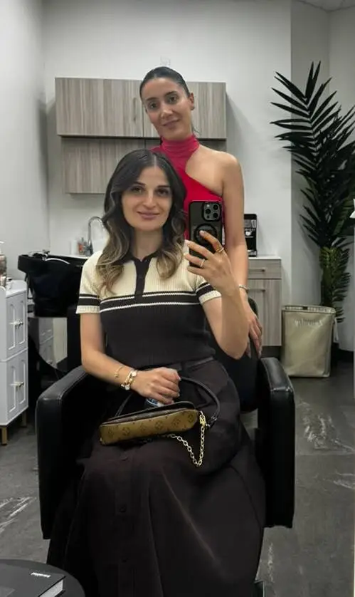 Client with soft brunette waves and honey highlights seated in the salon chair beside her stylist